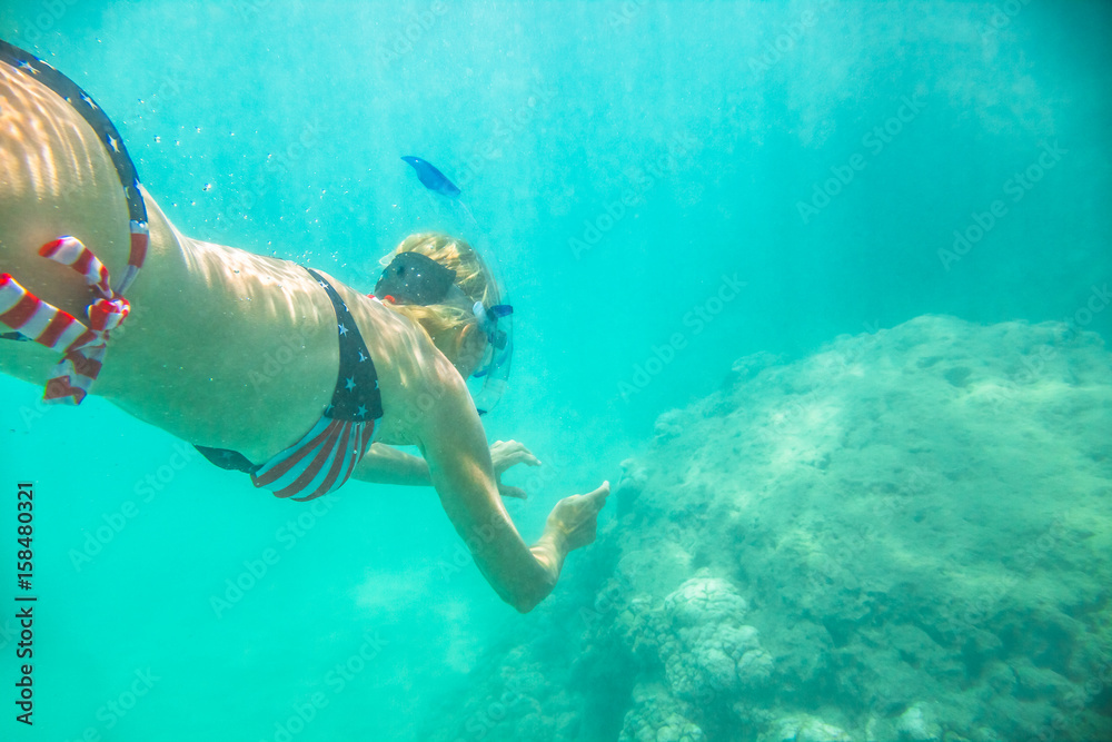 Woman snorkeler swims in tropical sea with american flag bikini. Underwater scene of a female apnea and doing skin diving. Watersport activity in Hawaii. Tropical destination holiday travel.