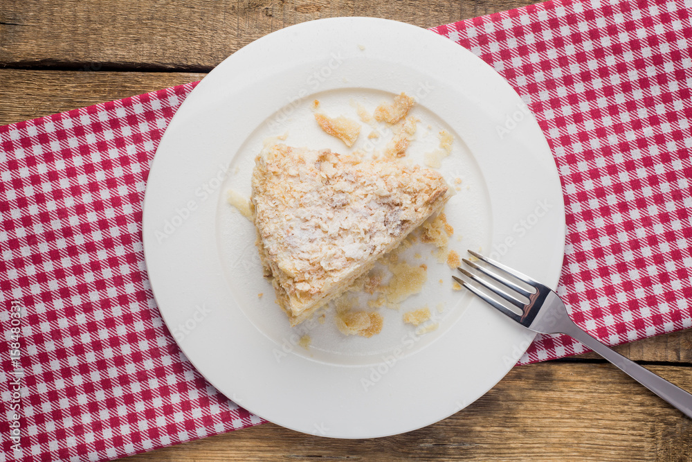 cake Napoleon on a white plate, on a wooden background and a red-white napkin cake Napoleon on a white plate, on a wooden background and a red-white napkin