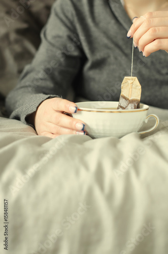 Female hands holding a cup of hot tea on warm blanket.