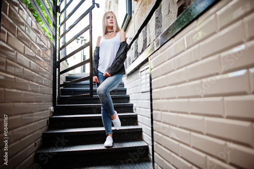 Stylish blonde woman wear at jeans, choker and leather jacket at street near stairs. Fashion urban model portrait.