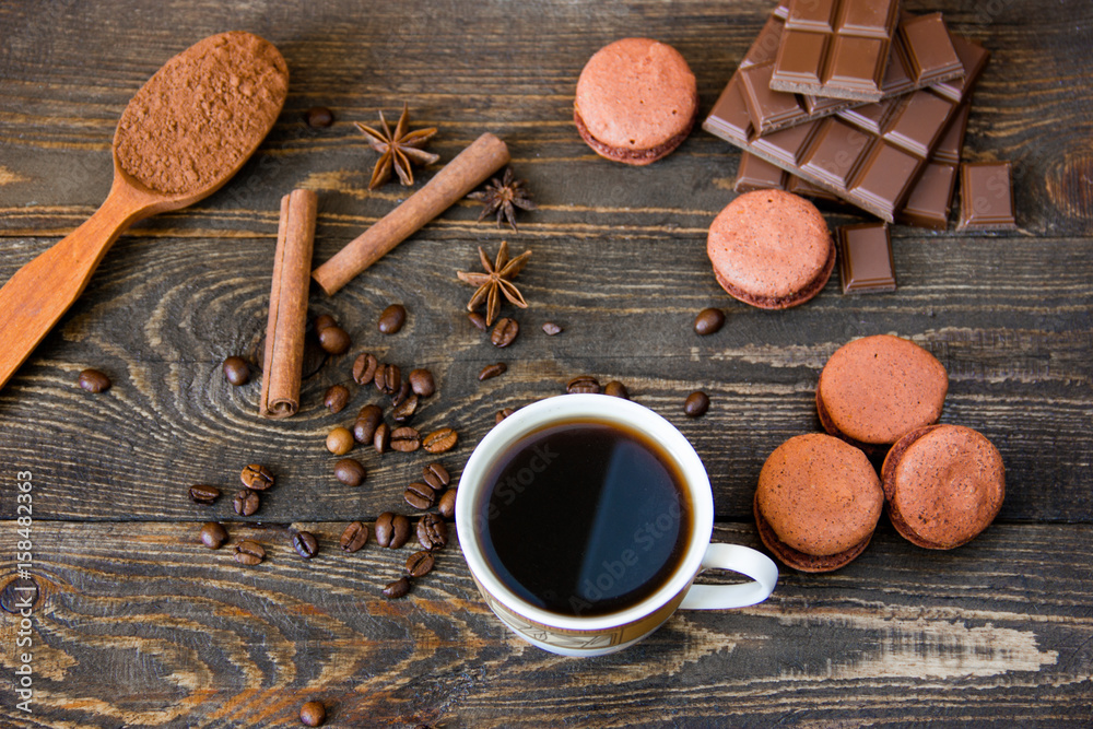 A cup of coffee with brown macaroons and chocolate on a wooden table