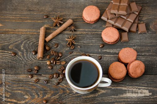 A cup of coffee with brown macaroons and chocolate on a wooden table
