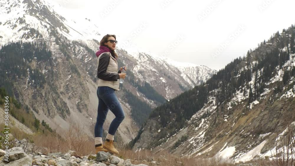 beautiful woman traveler drinks water on a background of beautiful mountains beautiful woman traveler drinks water on a background of beautiful mountains