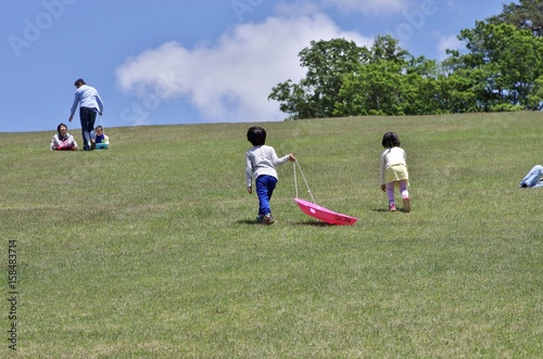 夏のスキー場の芝生でそり遊びをする子供
