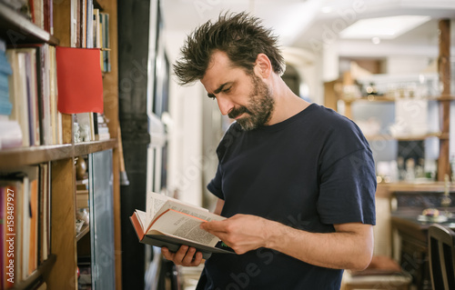 Obraz na plátně Curious man choosing book in his library at home