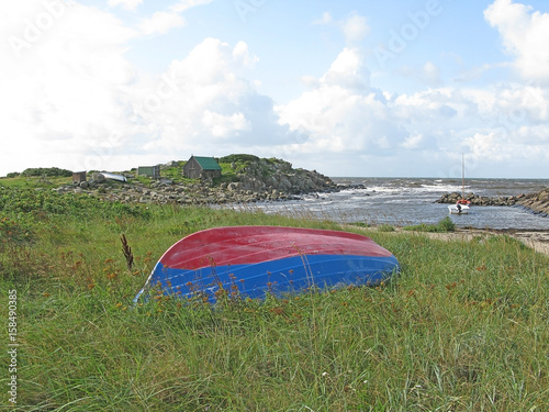 Natural landscape with red and blue boat in the grass at Skrea Strand on a sunny day with dark clouds in Falkenberg, Sweden.