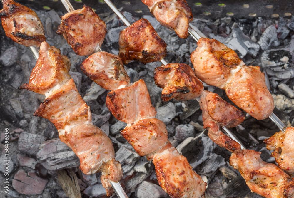 Pork meat cooking outdoor on skewers over smoldering carbon Pork meat cooking outdoor on skewers over smoldering carbon