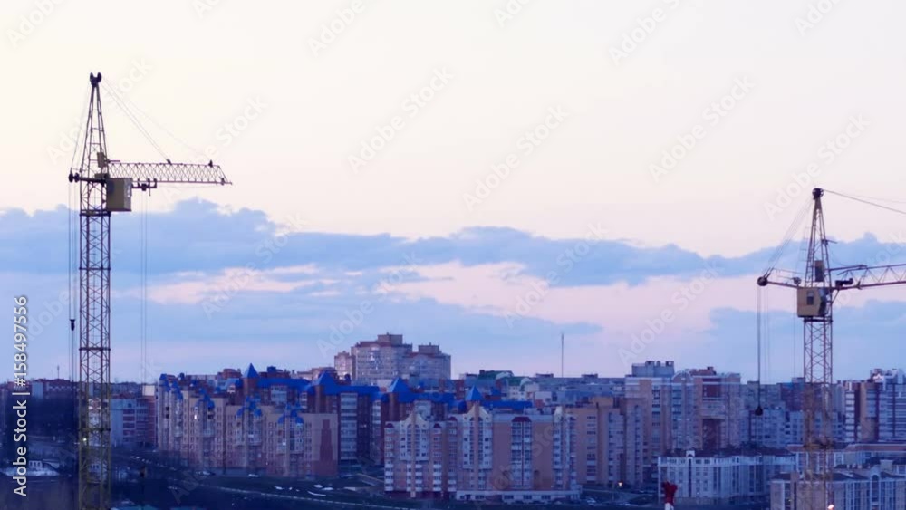 Crane working at sunset. Construction site with a city buildings on background. Timelapse. 4K. Crane working at sunset. Construction site with a city buildings on background. Timelapse. 4K.