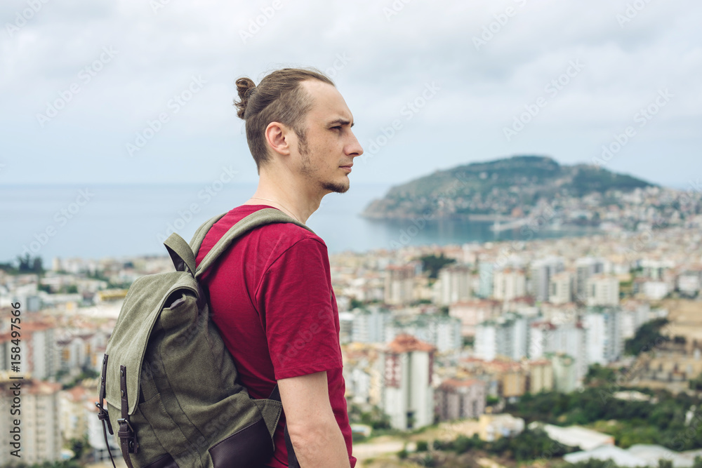 Man traveler with backpack explores the city looking at the panoramic view of the city and the coast. Man traveler with backpack explores the city looking at the panoramic view of the city and the coast.