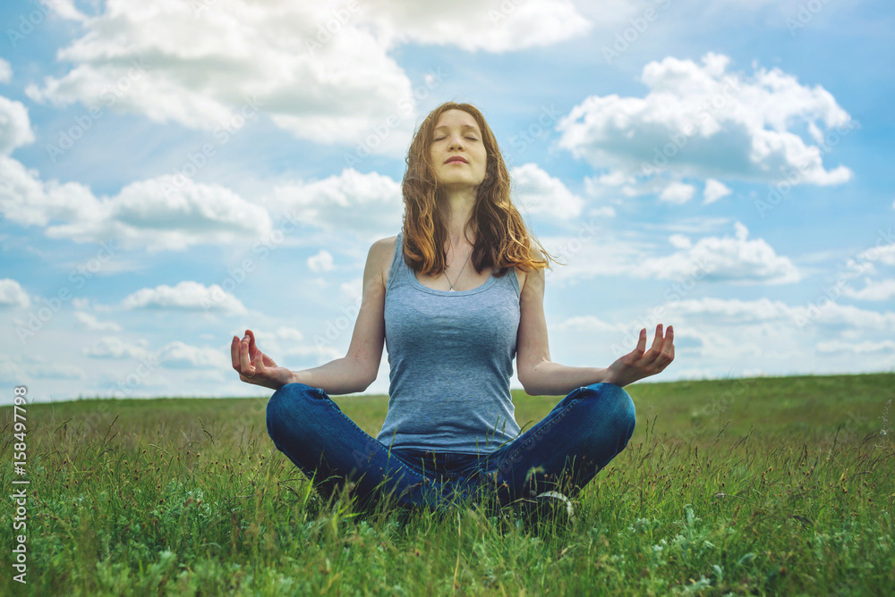 Woman traveler sitting on the meadow with green grass under blue sky with clouds in the Lotus position Woman traveler sitting on the meadow with green grass under blue sky with clouds in the Lotus position