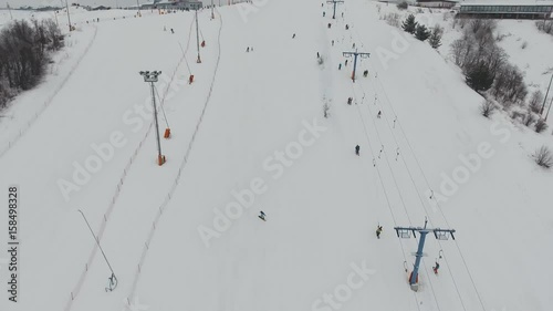 Aerial view: Skiers and snowboarders going down the slope in winter day. Skiers and snowboarders enjoying on slopes of ski resort in winter season. 4K video, aerial footage.