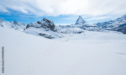 Scenic view on snowy Matterhorn peak in sunny day with blue sky and some clouds in background, Switzerland. © exzozis
