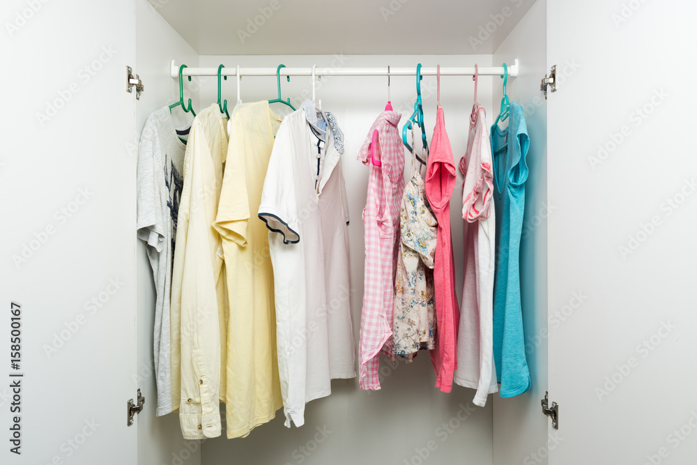 Clothes hanging on rail in white wardrobe. Men's and women's summer clothes, pastel colors
