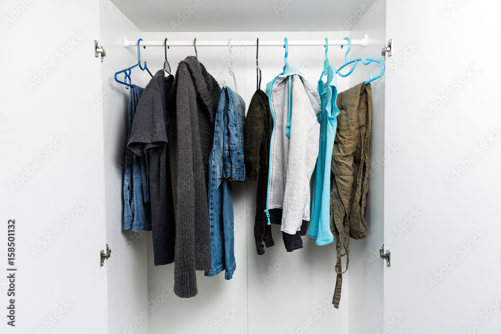 Clothes hanging on rail in white wardrobe. Men's and women's autumn or winter  clothes, grey and dark colors. Copy space