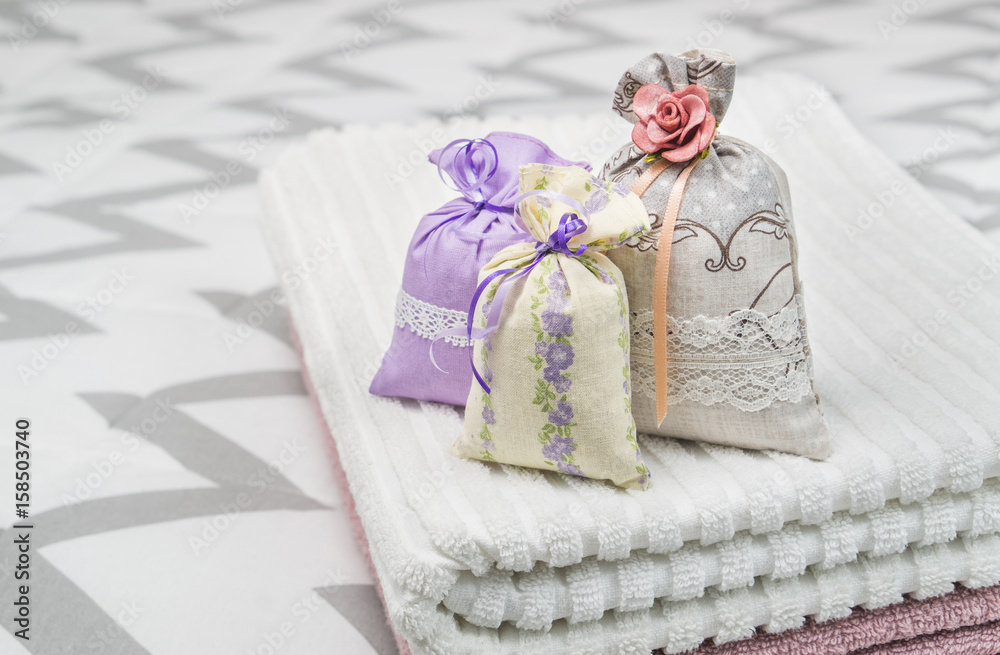 Three lavender scent pouches on towels. Scented sachets on bedroom bed. Fragrance bags for fresh home. Decoration, furnishing and storage accessories. Aromatic potpourri set. Three lavender scent pouches on towels. Scented sachets on bedroom bed. Fragrance bags for fresh home. Decoration, furnishing and storage accessories. Aromatic potpourri set.