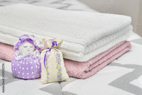 Scented pouch and lavender sachet figure and character representing a girl or woman. Dried lavender in decoration bags in bedroom and towels on bed. Aroma potpourri and furnishing items. © terovesalainen