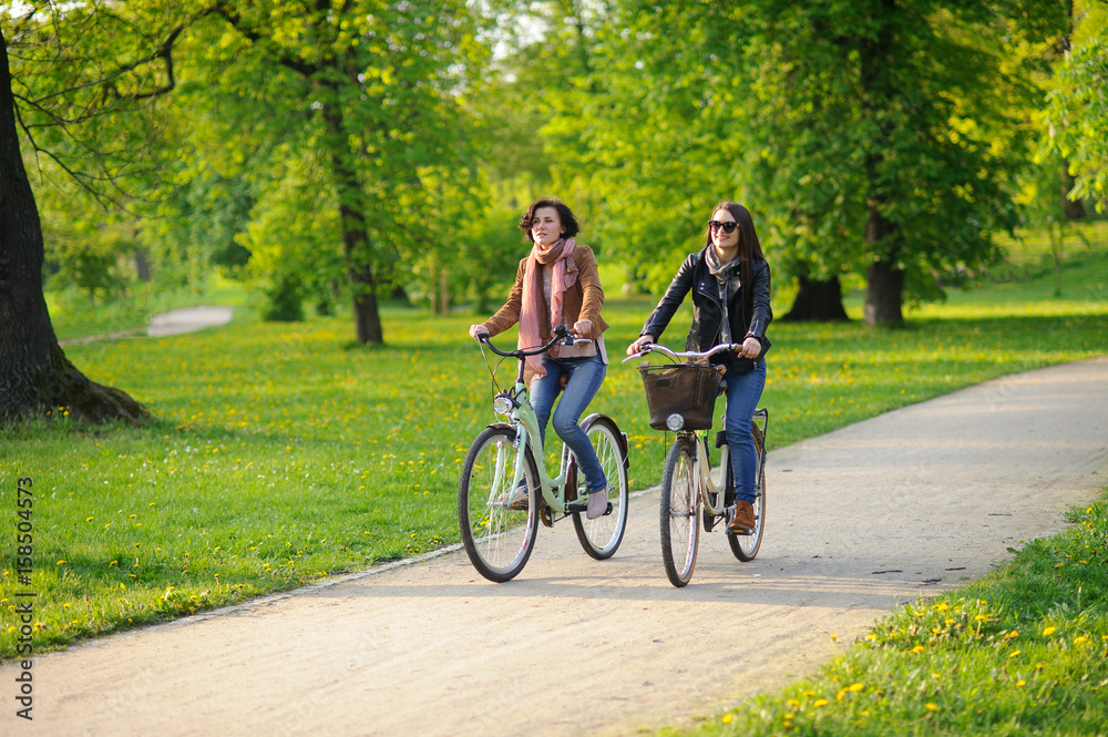 Two young attractive women ride bikes in the spring park. Two young attractive women ride bikes in the spring park.