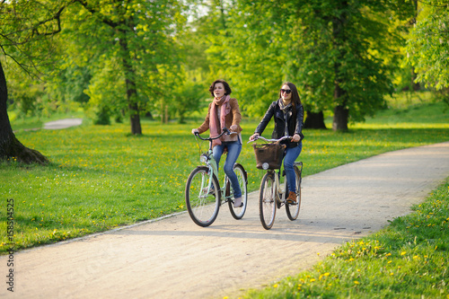 Two young attractive women ride bikes in the spring park.