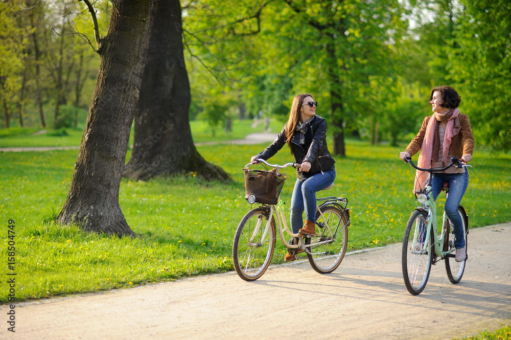 Fototapeta premium Two young attractive women ride bikes in the spring park.