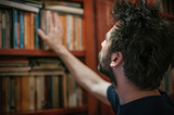 Curious man choosing book in his library at home
