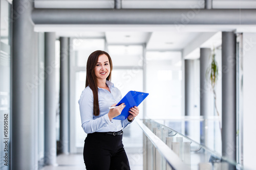 Beautiful business woman standing and holding paper board in modern business interior