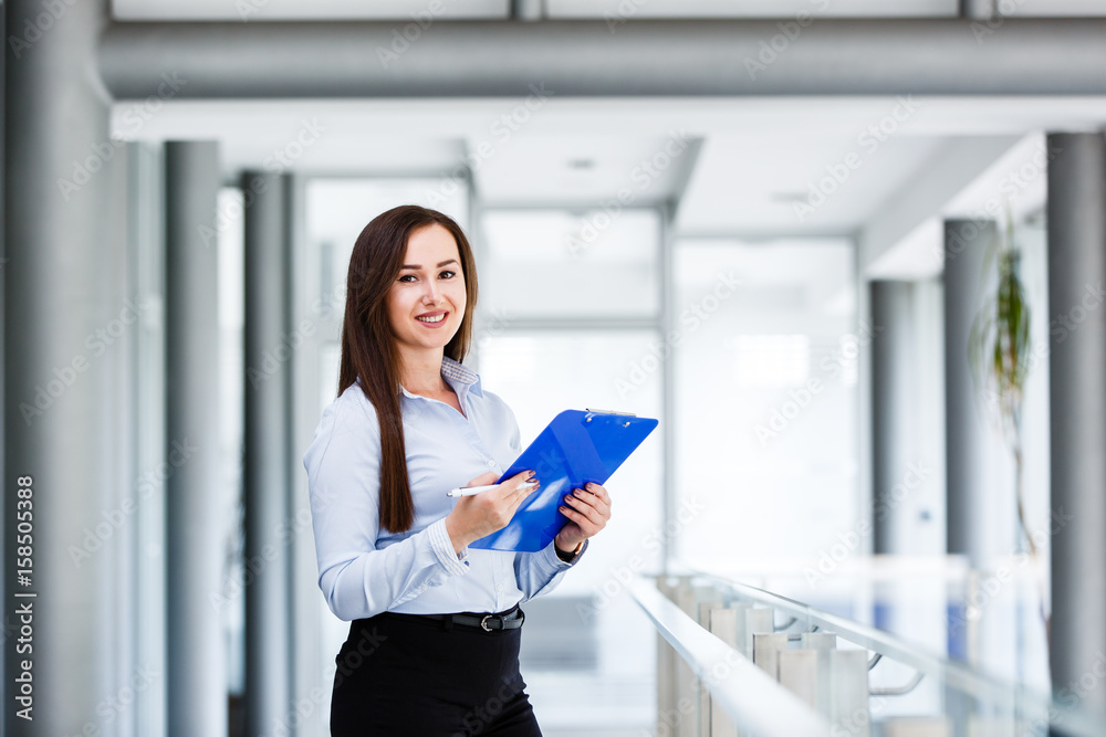 Beautiful business woman standing and holding paper board in modern business interior Beautiful business woman standing and holding paper board in modern business interior