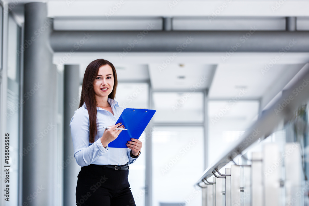 Beautiful business woman standing and holding paper board in modern business interior Beautiful business woman standing and holding paper board in modern business interior
