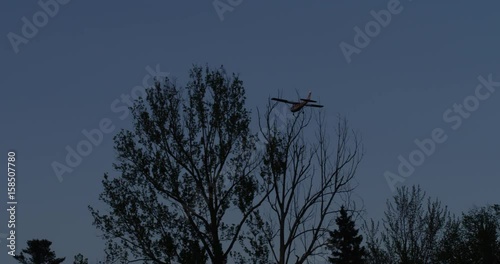 small red and white airplane flying at dusk prepares to land photo