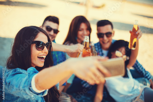 Happy young people having fun on the beach drinking beer and doing selfie