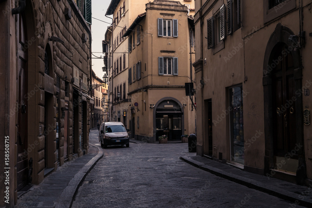 Narrow street and buildings with parked white van in Florence Italy, at dawn.