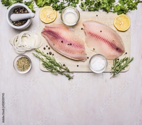raw fillet of tilapia with spices and herbs, lemon and pepper on a cutting board on a white background rustic village top view
