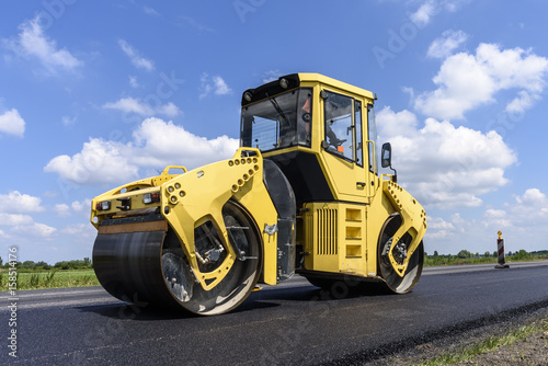 Workers groomed fresh asphalt road with yellow roller