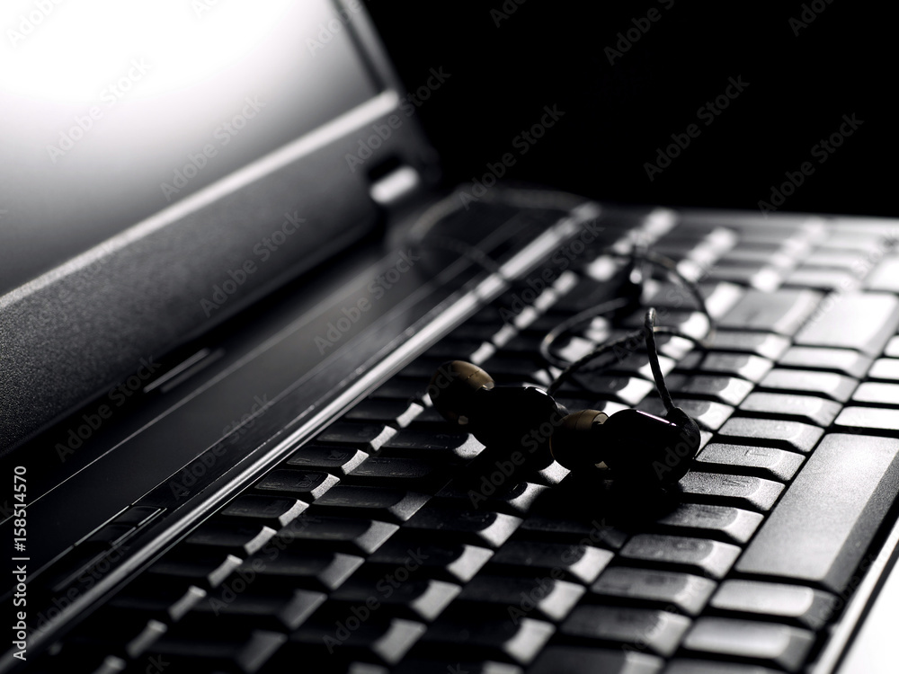 earphones on laptop keyboard under back light, low key