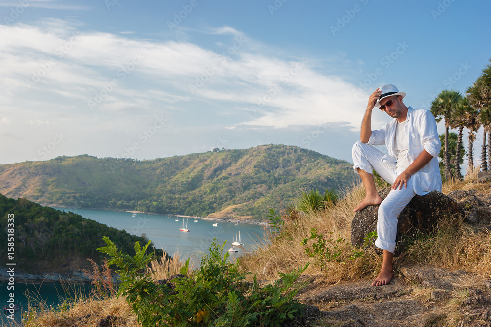 Naklejka premium young man sitting on a rock and looking at the sunset of Phuket