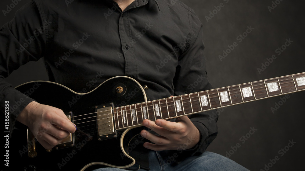 Man in shirt playing black electric guitar