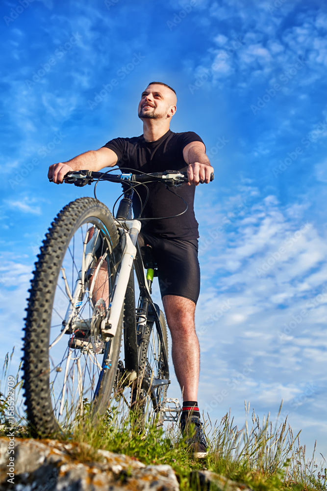 Bottom view of the smiling cyclist with bike against blue sky with clouds. Bottom view of the smiling cyclist with bike against blue sky with clouds.
