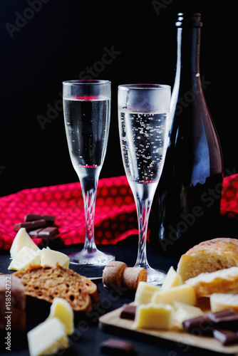 Alcoholic drinks, a holiday, white sparkling wine, glasses with champagne with freshly baked bread, mozzarella cheese and dark chocolate on a black wooden background 