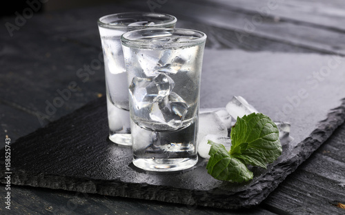 Vodka in shot glasses and ice on rustic wood background