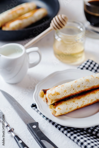 Traditional breakfast or lunch, in a hotel or restaurant, thin pancakes with cottage cheese, honey, coffee and milk on a white wooden background 