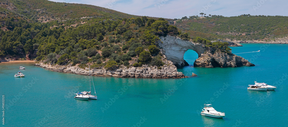 Panoramic view of San Felice bay with is natural arch (Architello) and anchored yachts on Vieste coast, Gargano, Apulia, Italy