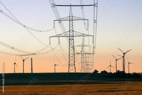 Green energy concept - high voltage power lines with the background of wind turbines farm