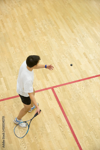 Young men playing match of squash/Squash player in action on squash court, back view