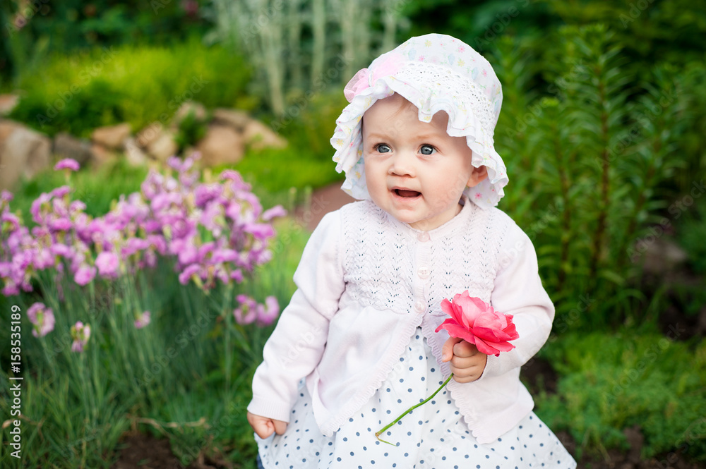 Girl 8 months old European Ukrainian little baby on a walk in the garden holds a flower and strawberries in her hands Girl 8 months old European Ukrainian little baby on a walk in the garden holds a flower and strawberries in her hands