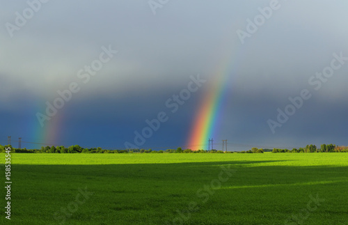 beautiful landscape with green meadow and a bright rainbow far away in the sky