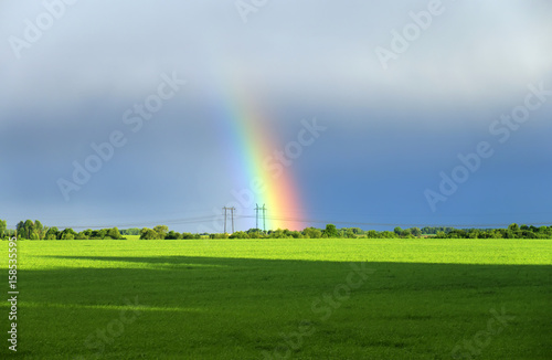 landscape with green meadow and a bright rainbow far away in the sky