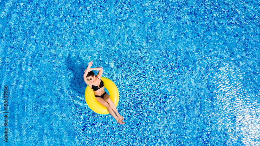 Vacation concept. Top view of slim young woman in bikini on the yellow air inflatable ring in the big swimming pool.