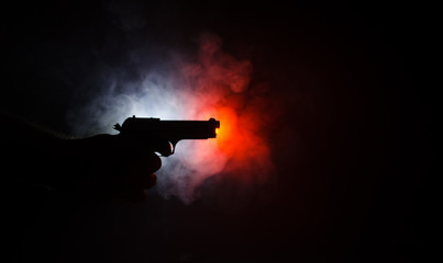 Male hand holding gun on black background with smoke ( yellow orange red white ) colored back lights, Mafia killer concept
