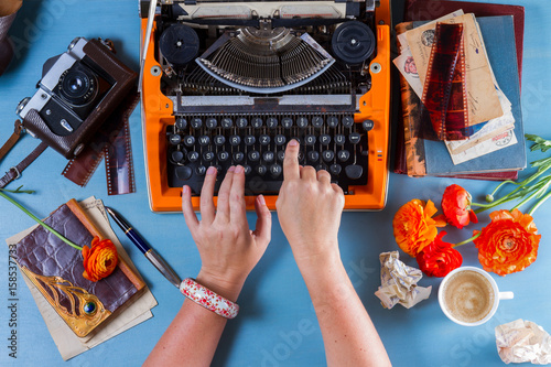 Workspace with someone hands typing on orange vintage typewriter on blue background