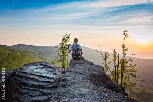 Man tourist sitting on top of hill at sunrise