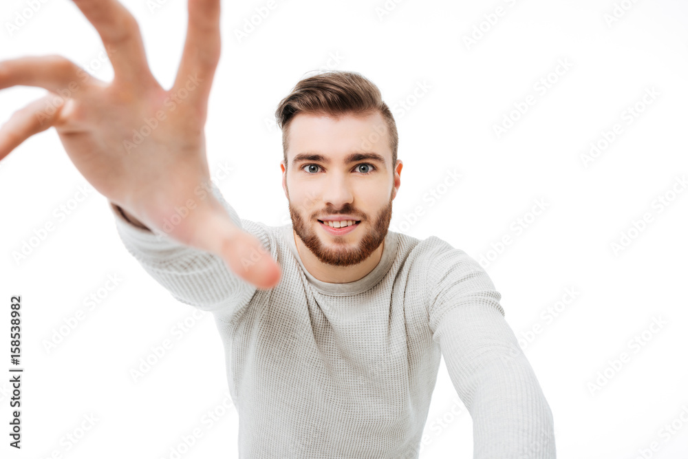 Handsome guy reaching out to the camera isolated. Young man trying to take your camera over white background Handsome guy reaching out to the camera isolated. Young man trying to take your camera over white background